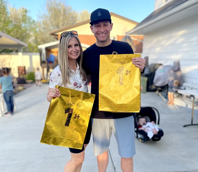 Two 2023 Quarter Mile Fitness champions holding gold first-place prize bags